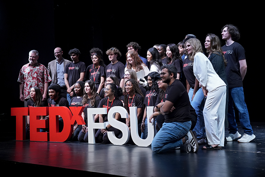 TEDxFSU committee members and speakers pose on stage behind the TEDxFSU letters at the 2025 conference. 